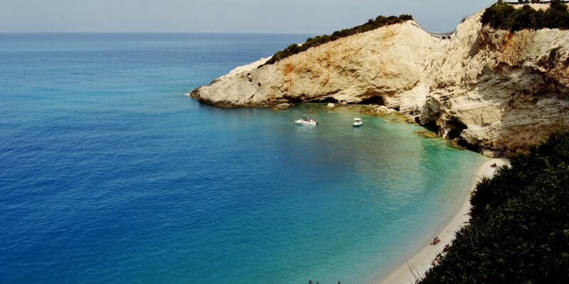 Das Bild zeigt Porto Katsiki, einen der bekanntesten Strände auf der griechischen Insel Lefkada. Der Strand besteht aus feinem, weißen Sand und wird von steilen, hellen Klippen umrahmt, die majestätisch in das türkisblaue Wasser ragen.