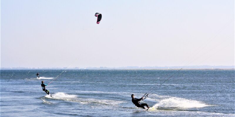 Drei Kitesurfer auf flachem Ostseewasser bei Fehmarn — die Insel zählt mit ihren windigen Bedingungen und flachen Buchten zu den bekanntesten Kitesurf-Spots an der deutschen Ostseeküste