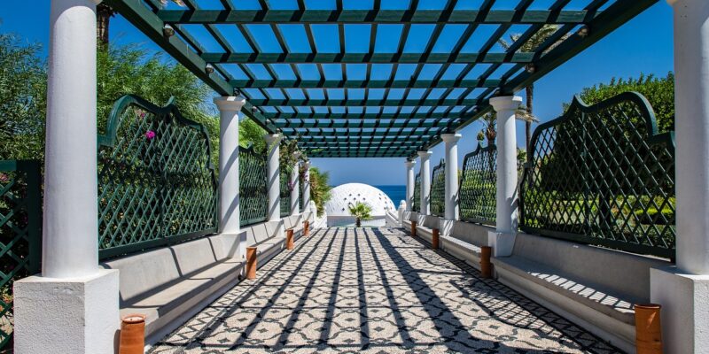 Kallithea-Thermen Rhodos: Pergola mit Mosaikboden Pergola der historischen Kallithea-Therme auf Rhodos mit charakteristischem Hochlakia-Kieselmosaik aus schwarzen und weißen Steinen, weißen Säulen, grün-weißem Holzgitter und dem Rotunden-Pavillon der Therme im Hintergrund mit Blick auf das Mittelmeer