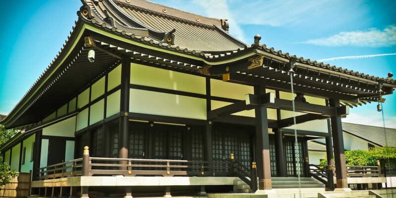 EKŌ-Haus Japanischer Tempel im traditionellen Baustil mit geschwungenem Ziegeldach und dunklem Holzrahmen vor blauem Himmel.