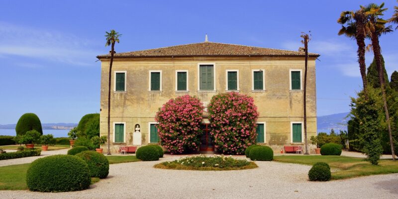 Historische Villa in Punta San Vigilio mit Palmen, blühenden Sträuchern, gepflegtem Garten und Blick auf den Gardasee