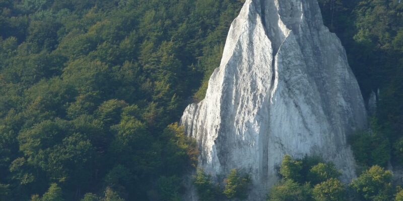 Bei Sonnenaufgang erhebt sich der majestätische Königsstuhl aus den Feldern, eine atemberaubende Felsformation mit einem Pfad, der sich in der Nähe entlangschlängelt, umarmt von den Hügeln in der Ferne unter einem klaren Himmel.