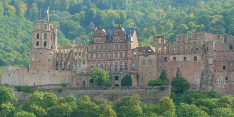 Schloss Heidelberg, ein majestätisches Schloss mit einer Mischung aus gotischer und Renaissance-Architektur, ist von üppigen grünen Wäldern umgeben. Sein kompliziertes Design und seine hohen Türme heben sich vor dem Hintergrund des dichten Laubes und des klaren Himmels ab.