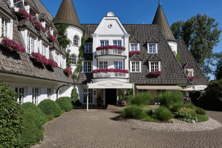 Weiße Hotelfassade mit Türmen, Blumenschmuck und rundem Vorplatz
