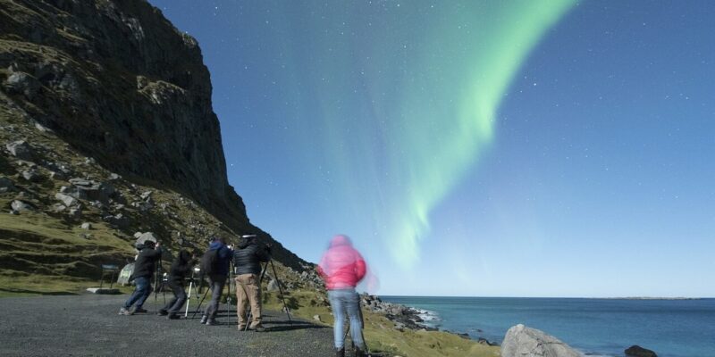 Fotografen auf den Lofoten filmen das grüne Naturschauspiel der Polarlichter, ausgelöst durch Sonnenaktivität , während die Berge nahe Tromsø im Hintergrund aufragen.