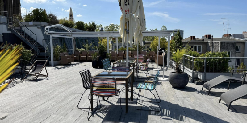 Mauritius Hotel Köln Dachterrasse Sonnige Dachterrasse des Mauritius Hotels in Köln mit bunten Stühlen, Tischen, Liegestühlen und Blick über die Stadt.