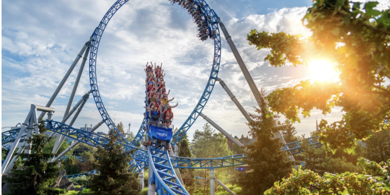 Der blaue Achterbahnzug der 'blue fire' fährt mit erhobenen Händen der Passagiere durch einen riesigen Looping vor einem leicht bewölkten Himmel im Europa-Park.