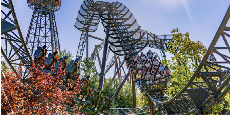 Ein voll besetzter Zug der Achterbahn 'Voltron Nevera' schießt im Europa-Park durch eine enge Kurve, im Hintergrund ist ein markanter Wardenclyffe-Tower im Tesla-Stil zu sehen.